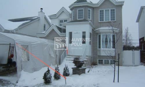 Maison grise sou la neige avec un abris d'auto double devant
